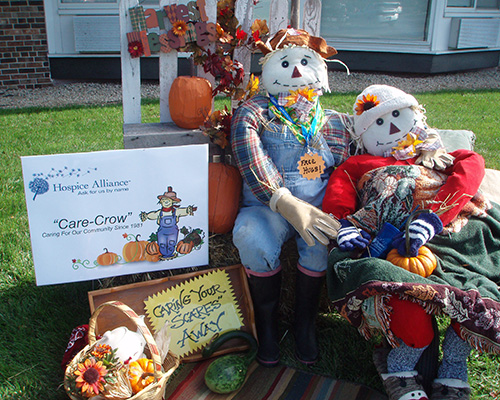 Two scarescrows sitting next to a sign that says "Care-Crow" Caring for our community since 1981