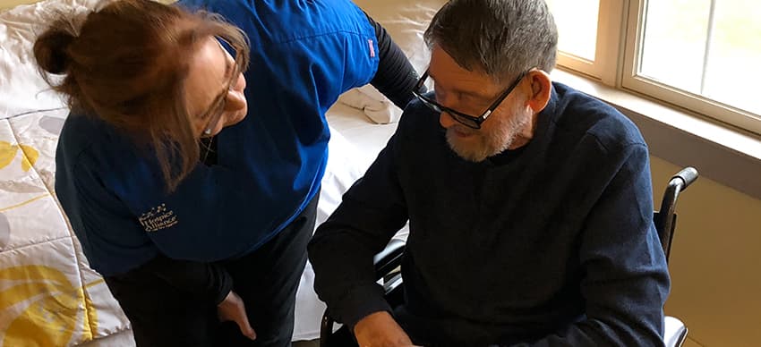 Hospice nurse standing next to an older male patience sitting in an wheel chair