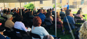 Crowd of people sitting under a tent listening to a person speaking at a podium
