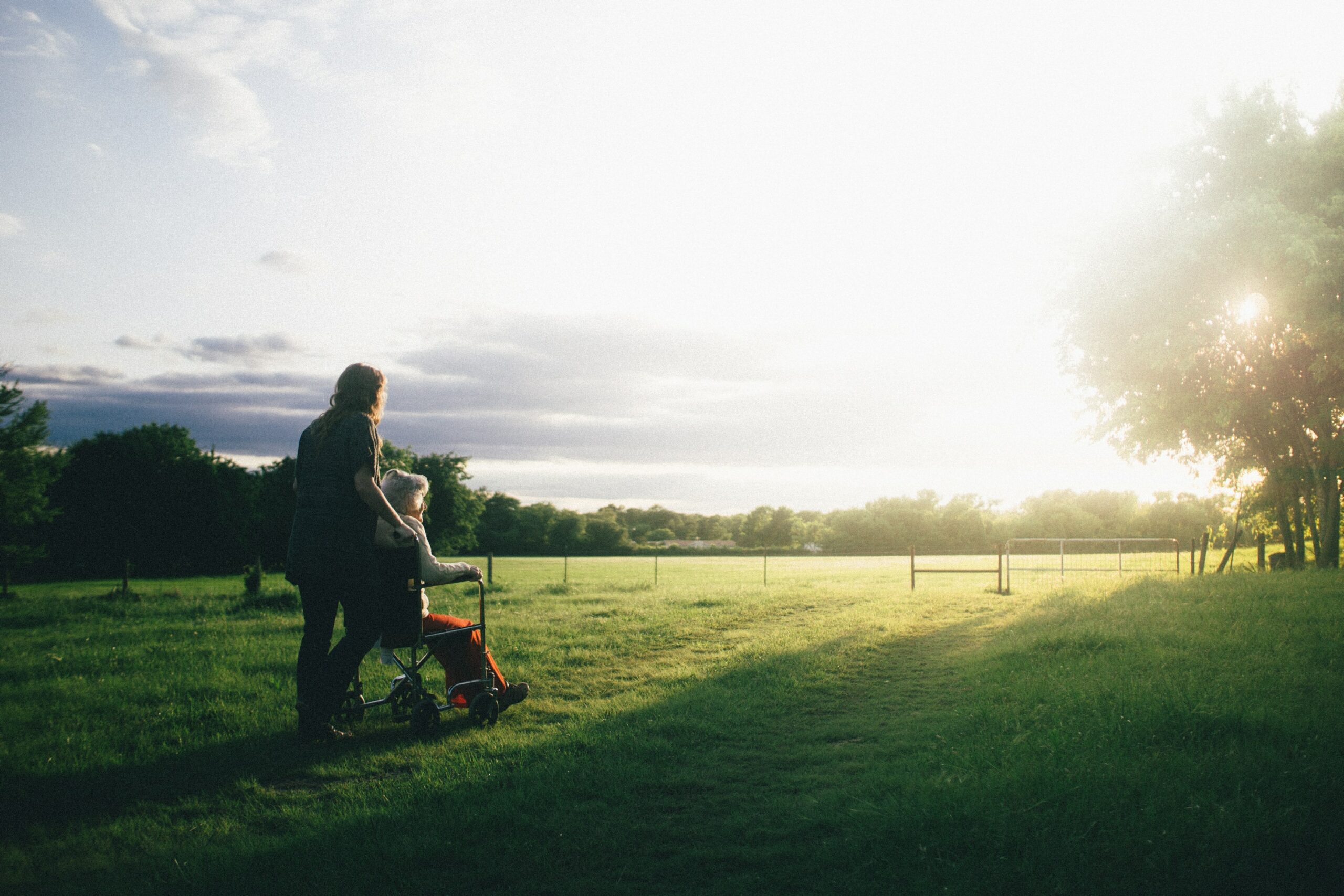 Empathy - Woman on a walk with elderly woman in wheelchair through grass field